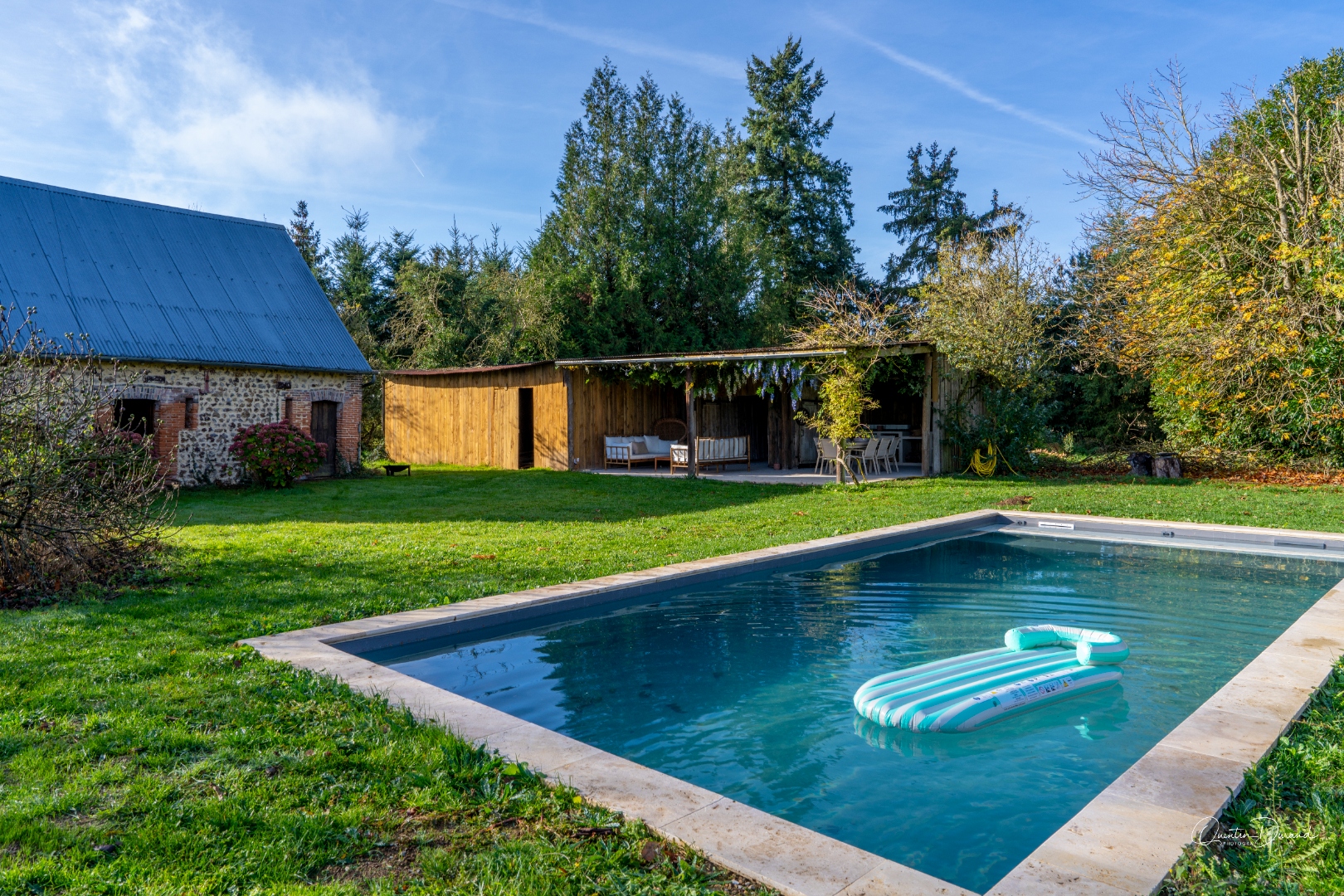 Piscine 9x4m avec bouée, entourée de verdure et pergola en arrière-plan