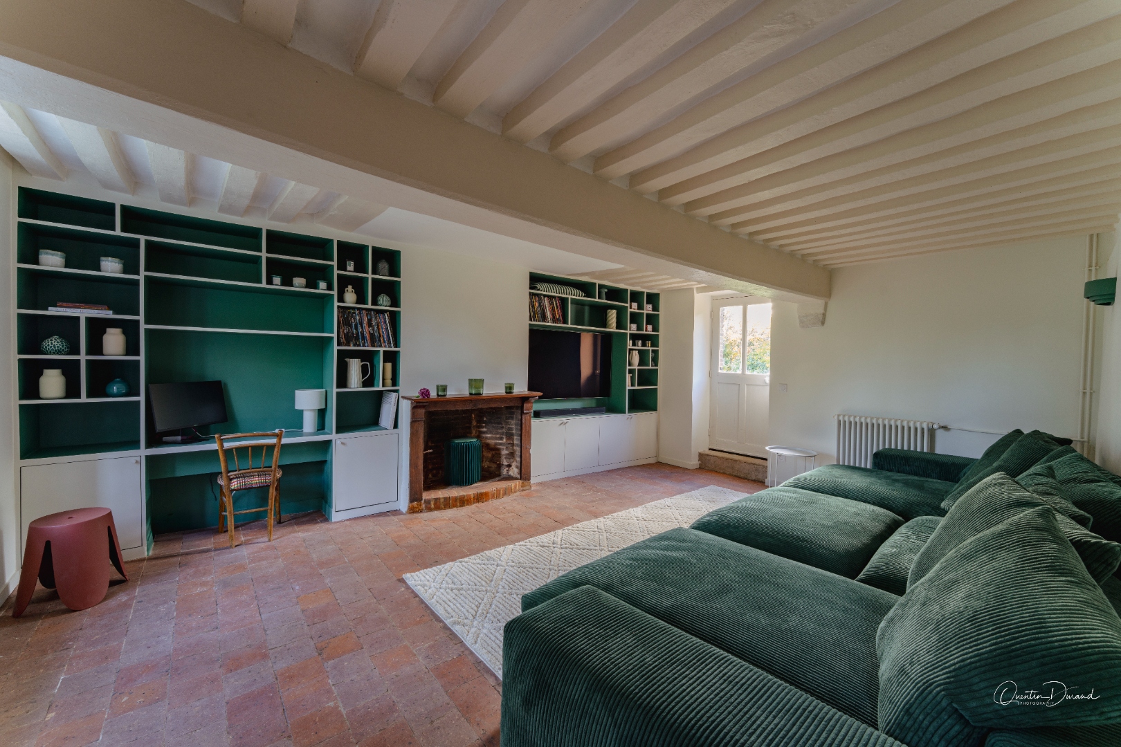 Salle TV avec grand canapé vert, bibliothèque et cheminée